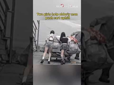 Two girls help elderly man push cart uphill